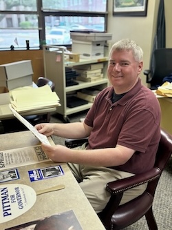 Brandon Ball sits a table with pieces from the collection. He is holding two letters, typed on white paper