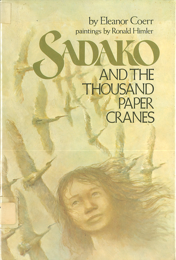 Cover of the book Sadako and the Thousand Paper Cranes by Eleanor Coerr with paintings by Ronald Himler. The cover features the painting of a young woman with cranes flying overhead. 